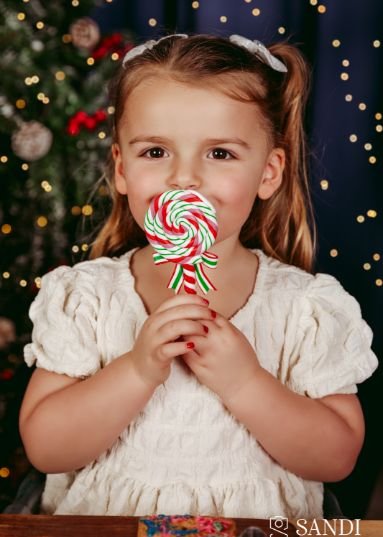 A happy girl holding a giant lollipop in a beautiful portrait from a Sandi Studio Christmas mini session in Dorchester, featured in our client reviews.