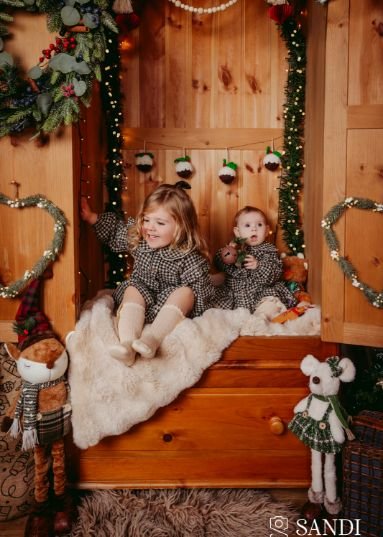 A toddler and a baby sitting together inside the decorated Magic Wardrobe set during their whimsical Christmas mini session in Dorchester.